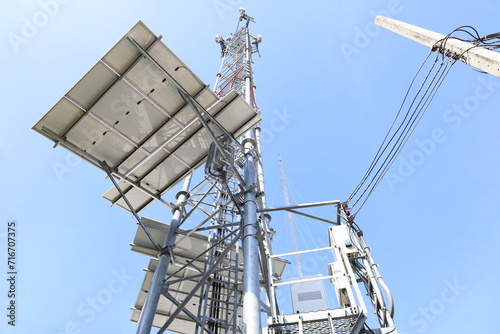 Repeater base with solar panels. Telecommunications base station and photovoltaic and electrical systems in bottom view on blue sky background with copy space. Selective focus