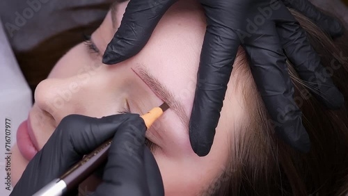 Applying a pencil sketch to the eyebrow contour before the treatment. Permanent makeup procedure, performing PMU of eyebrows photo