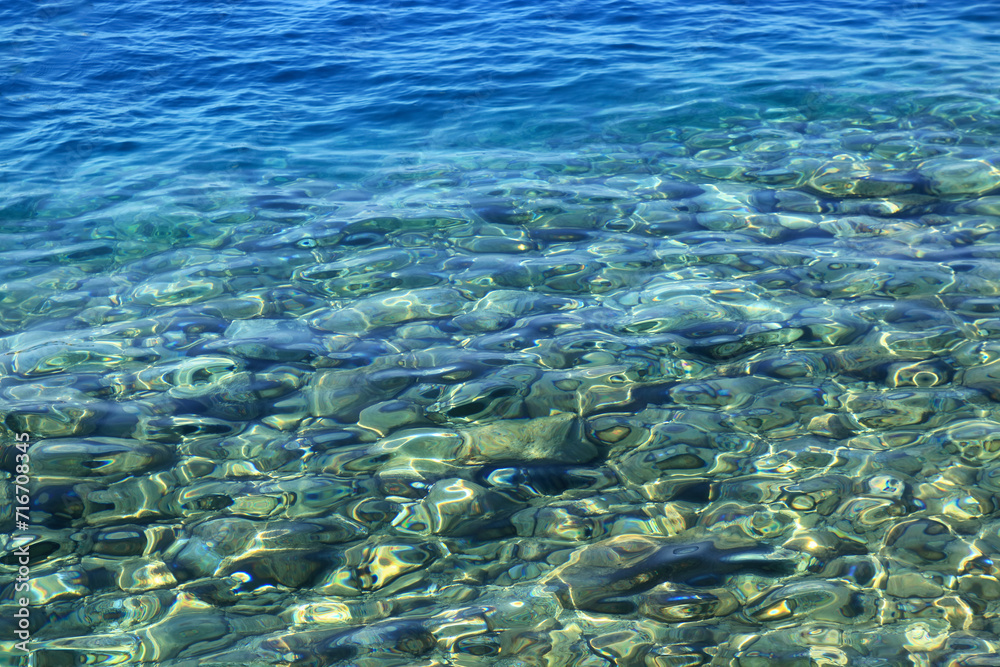 Fototapeta premium Abstract nature background. Backdrop. Wallpaper of little pebbles or stones in sea water. Pebbles under water. Nautical background. Clean sea water. Transparent sea. Beach summer background.