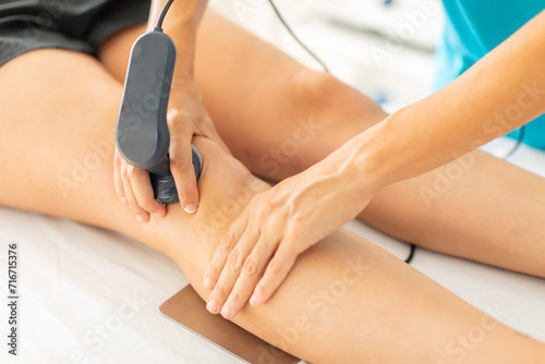 A physical therapist applies radiofrequency waves with a diathermy machine to relieve her patient's knee muscle pain