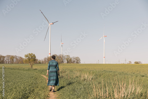 Woman in blue dress walking along a small road towards wind turbine fields outside Brandenburg germany © Amparo Garcia