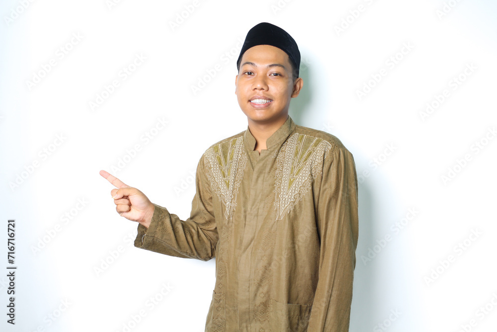 asian muslim man pointing to the right side and smiling at camera wearing islamic dress isolated on white background asian muslim man pointing to the right side and smiling at camera wearing islamic dress isolated on white background