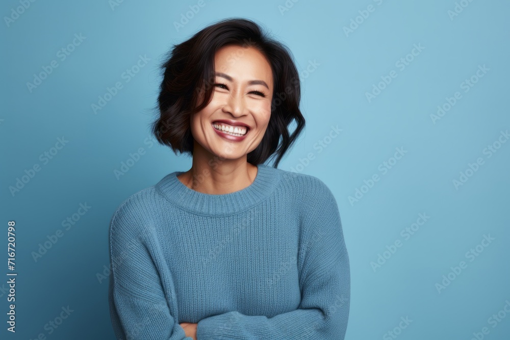 Portrait of a cheerful asian woman in her 40s wearing a cozy sweater against a soft blue background. AI Generation Portrait of a cheerful asian woman in her 40s wearing a cozy sweater against a soft blue background. AI Generation