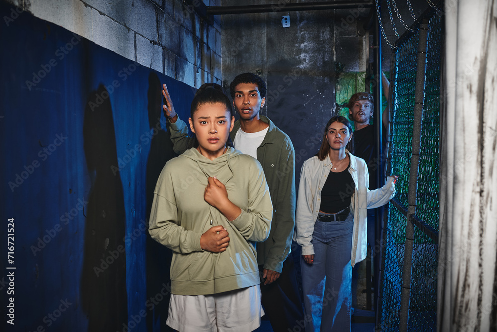 young and multicultural friends walking through secret passage in quest room, adventure and mystery