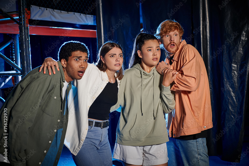 four diverse and scared young people looking at something while discovering a clue in escape room