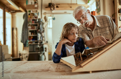 Grandfather and grandson working on a model boat in a woodworking workshop photo