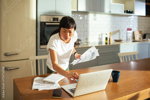 Young Asian woman paying bills online on a laptop at home photo