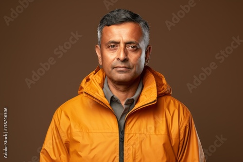 Portrait of a satisfied indian man in his 50s wearing a lightweight packable anorak against a soft brown background. AI Generation © CogniLens
