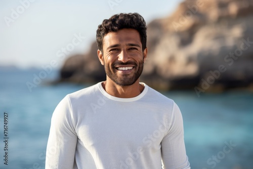 Portrait of a grinning indian man in his 20s wearing a classic turtleneck sweater against a serene seaside background. AI Generation