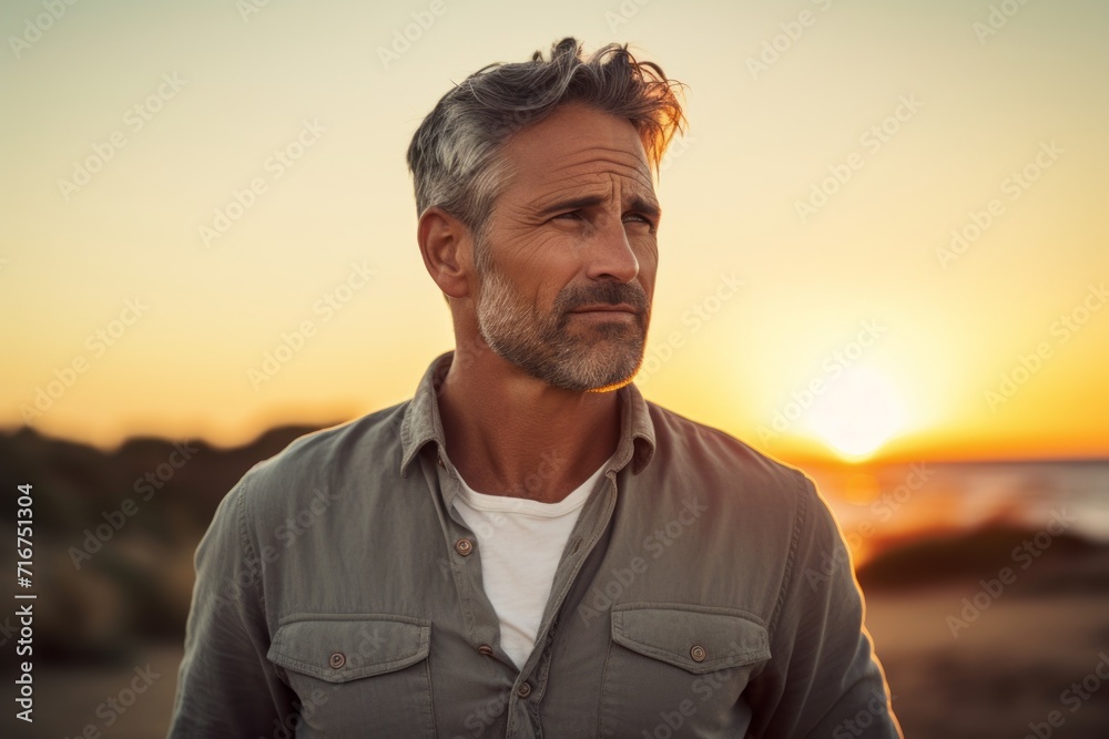 Portrait of a tender man in his 50s sporting a versatile denim shirt against a stunning sunset beach background. AI Generation