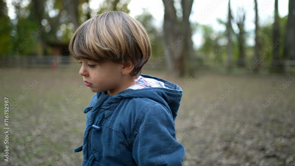 Sad pensive child walks forward outside at park during fall season. Thoughtful kid in great outdoors feeling worry Sad pensive child walks forward outside at park during fall season. Thoughtful kid in great outdoors feeling worry