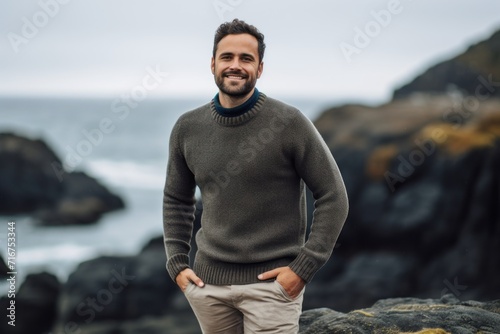 Portrait of a merry man in his 30s wearing a cozy sweater against a rocky shoreline background. AI Generation