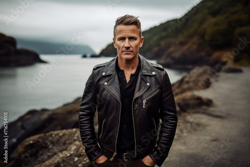 Portrait of a happy man in his 40s sporting a classic leather jacket against a rocky shoreline background. AI Generation