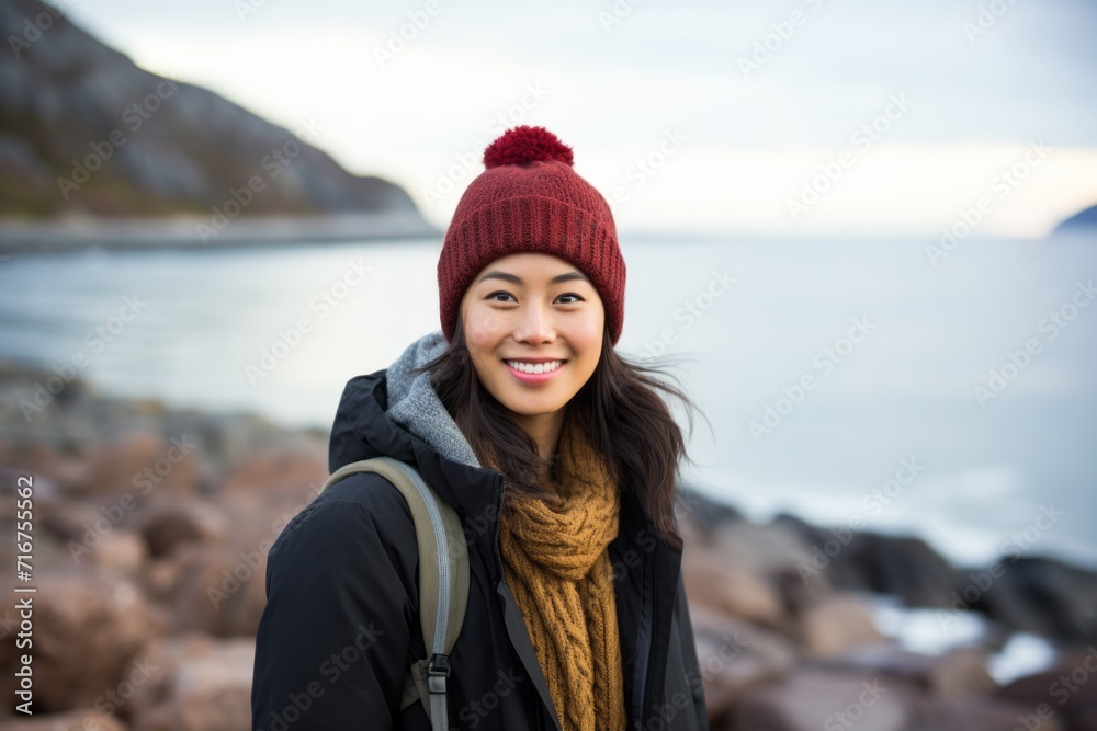 Portrait of a blissful asian woman in her 20s dressed in a warm ski hat against a rocky shoreline background. AI Generation Portrait of a blissful asian woman in her 20s dressed in a warm ski hat against a rocky shoreline background. AI Generation