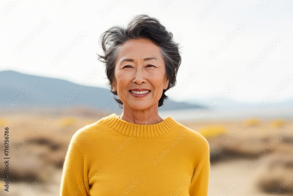 Portrait of a grinning asian woman in her 70s showing off a thermal merino wool top against a serene dune landscape background. AI Generation Portrait of a grinning asian woman in her 70s showing off a thermal merino wool top against a serene dune landscape background. AI Generation