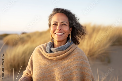 Portrait of a smiling indian woman in her 50s wearing a cozy sweater against a serene dune landscape background. AI Generation photo