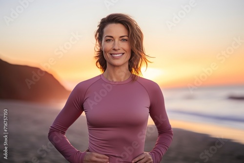 Portrait of a content woman in her 30s showing off a thermal merino wool top against a vibrant beach sunset background. AI Generation