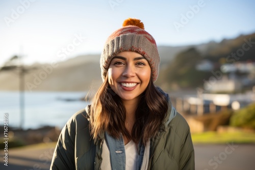Portrait of a happy indian woman in her 30s sporting a trendy beanie against a beautiful coastal village background. AI Generation © CogniLens