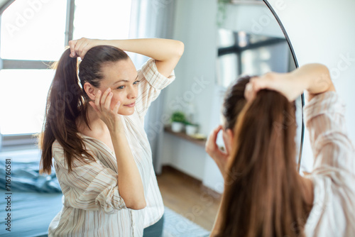 Woman styling her ponytail in the mirror at home photo