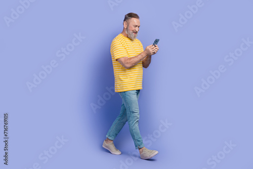 Full body profile photo of nice positive person walk use smart phone typing blog post isolated on violet color background