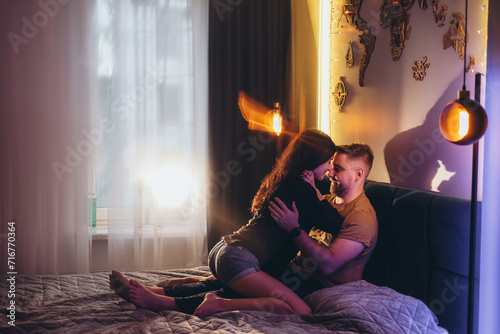 A couple of a guy and a girl on a bed in a room lit with colored warm light. The girl sits sexy on top of the guy. World map on the wall
