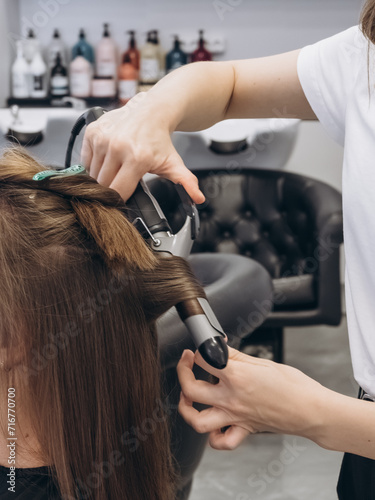 The hairdresser twists hair with a curling iron. Creating curls