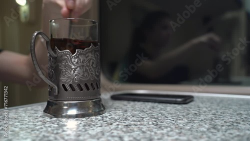 Closeup of a glass with a cup holder for hot tea stands on a table in a reserved carriage of a passenger train. It is stirred with a spoon and drunk from it photo