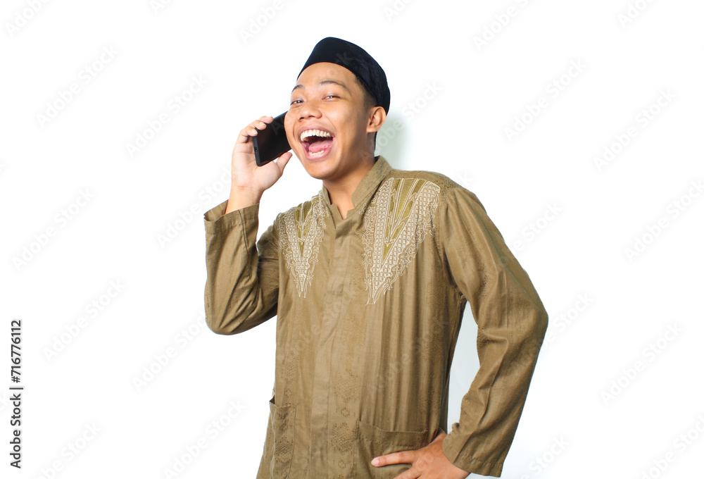excited asian muslim man speaking using mobile phone with hand on waist isolated on white background, looking at camera excited asian muslim man speaking using mobile phone with hand on waist isolated on white background, looking at camera