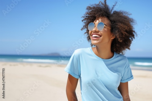 Portrait of young african american woman with curly hair at beach. Smiling black woman walking at the seaside.