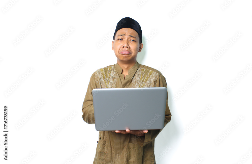 sad asian muslim man holding laptop with crying expression isolated on white background sad asian muslim man holding laptop with crying expression isolated on white background