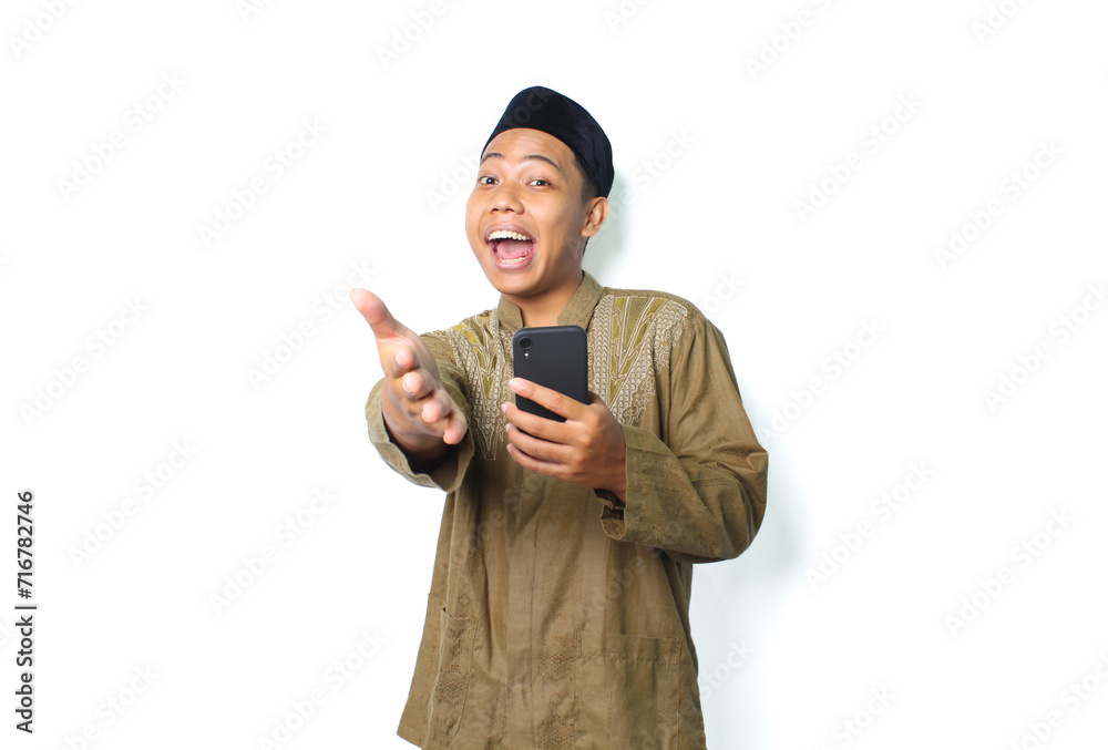 funny asian muslim man holding smartphone and offering handshake at camera isolated on white background funny asian muslim man holding smartphone and offering handshake at camera isolated on white background