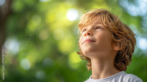 Young boy gazing into the lush greenery of a forest, bathed in soft natural light that filters through the leaves creating a peaceful atmosphere.