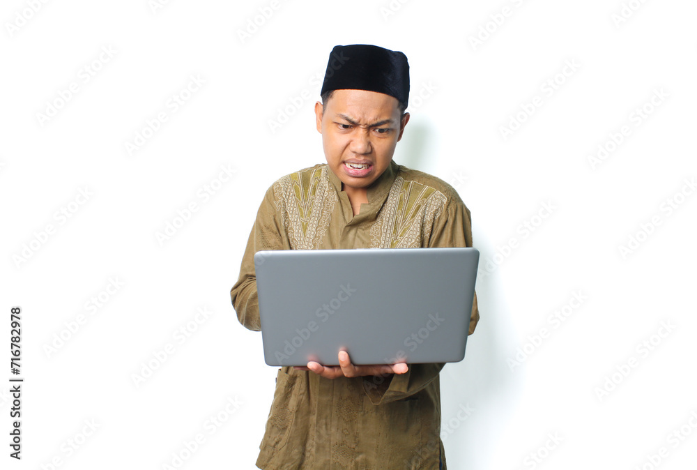asian muslim man holding laptop with angry expression wearing islamic dress isolated on white background asian muslim man holding laptop with angry expression wearing islamic dress isolated on white background