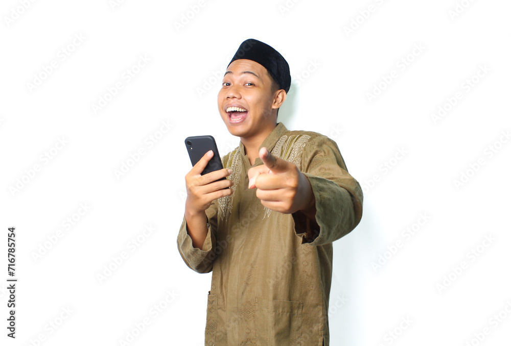 funny asian muslim man screaming while pointing at camera with holding moblie phone isolated on white background funny asian muslim man screaming while pointing at camera with holding moblie phone isolated on white background