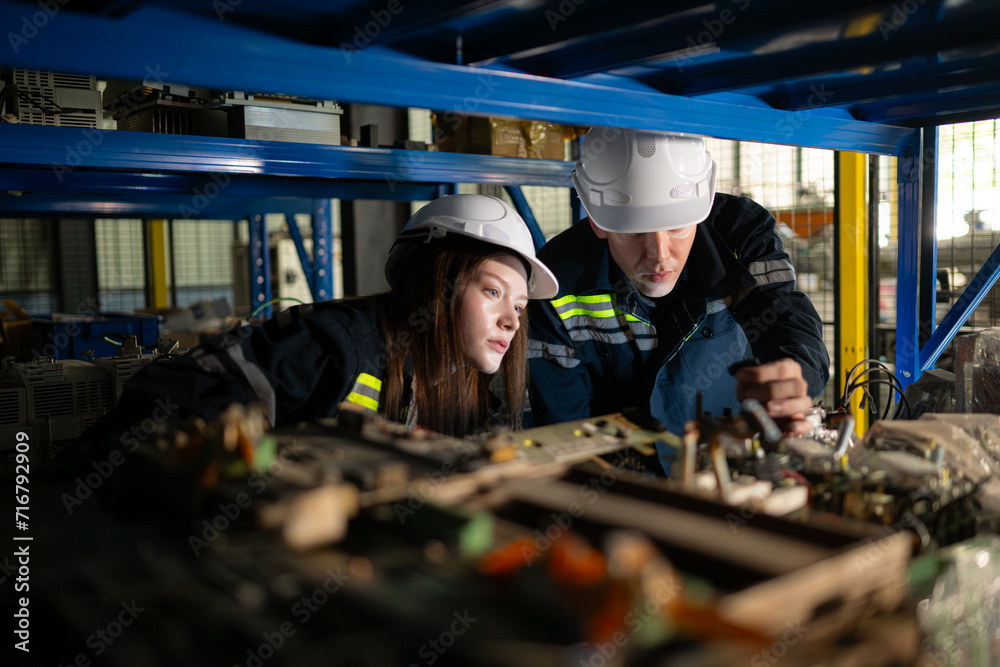 A young female engineer and a male supervisor work together in robotic arm spare parts warehouse, Robotic arm industry and engineering concept.
