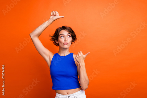 Photo of uncertain doubtful lady wear blue singlet looking showing two thumbs empty space isolated orange color background