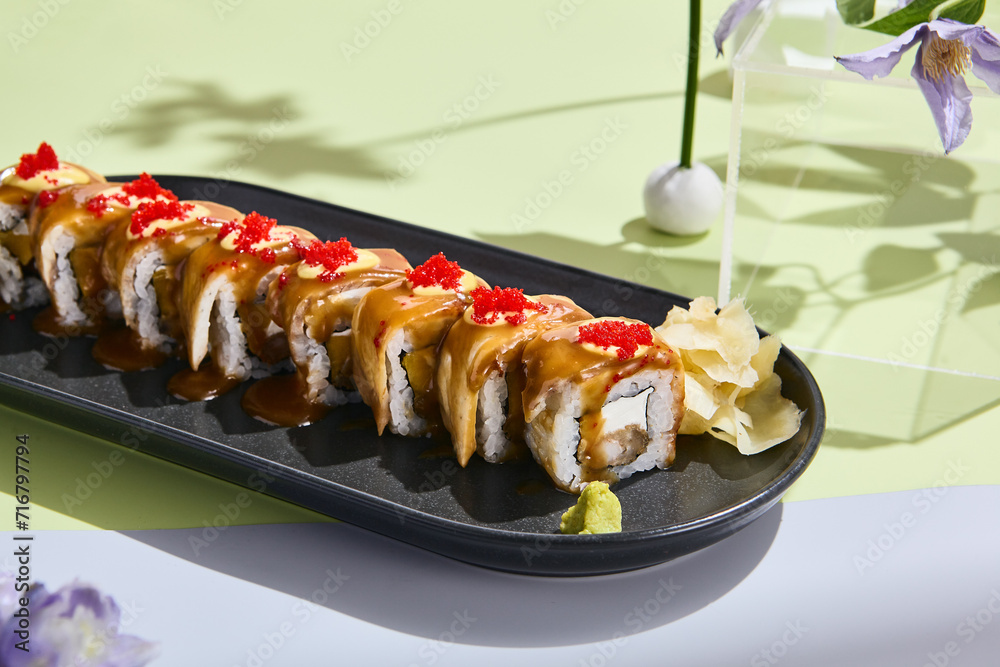 Summery sushi concept with eel roll, tobiko caviar, and unagi sauce amidst pastel floral decor Summery sushi concept with eel roll, tobiko caviar, and unagi sauce amidst pastel floral decor