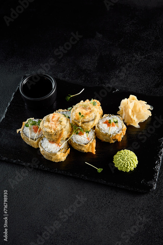 Salmon tempura roll on a textured black slate with condiments