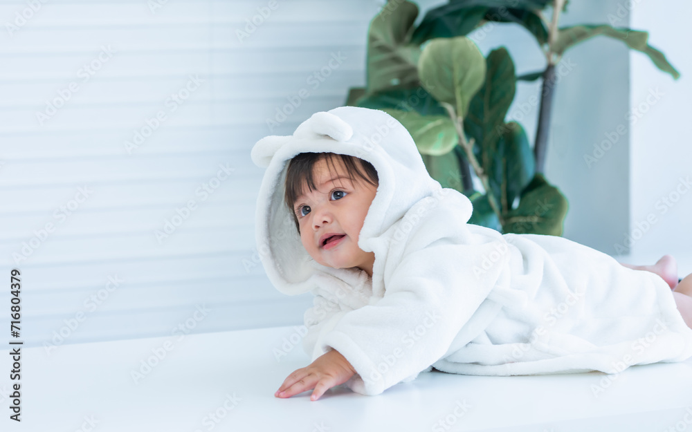 Adorable caucasian little baby daughter girl, wearing cute white bathrobe, taking bath in morning, sitting in baby bathtub, laughing, smiling with happiness at home or house. Kid Development Concept. Adorable caucasian little baby daughter girl, wearing cute white bathrobe, taking bath in morning, sitting in baby bathtub, laughing, smiling with happiness at home or house. Kid Development Concept.