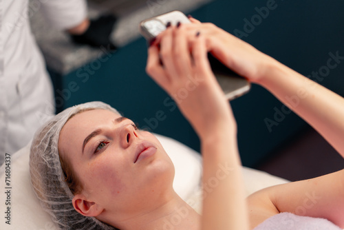 girl lying on a couch in a beauty salon taking a photo of her face after a cosmetic procedure