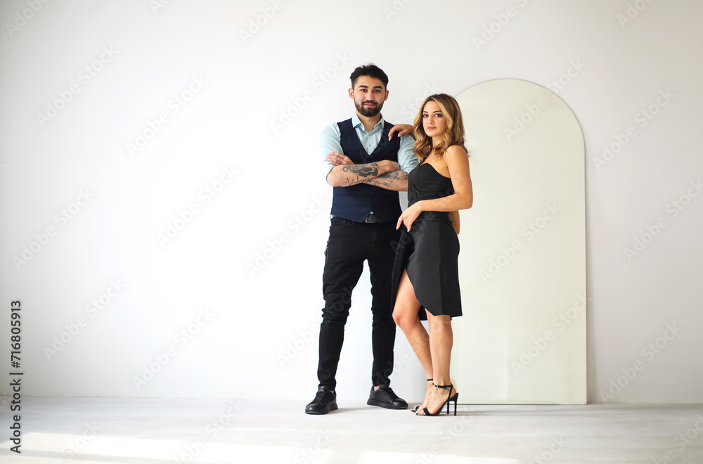 Stylish young ethnic couple embracing against dark gray wall background looking to camera thoughtfully. Portrait of the couple Stylish young ethnic couple embracing against dark gray wall background looking to camera thoughtfully. Portrait of the couple