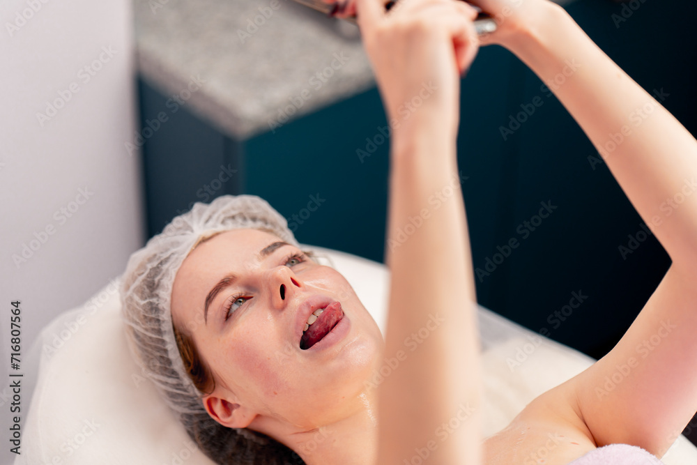 Fototapeta premium a girl lies on sofa in beauty salon taking a photo of her face with gel during a cosmetic procedure