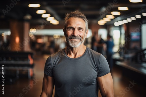 Portrait of a happy man in his 40s wearing a rugged jean vest against a dynamic fitness gym background. AI Generation