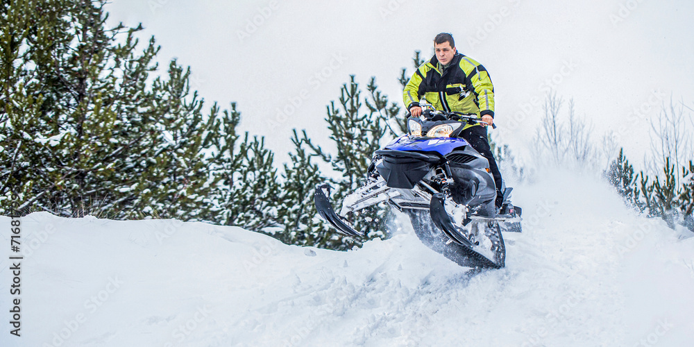 Athlete on a snowmobile moving in the winter forest in the mountains. Man and fast action snowmobile jumping. Jumping on a snowmobile on a background of winter forest. Bright snowmobile Athlete on a snowmobile moving in the winter forest in the mountains. Man and fast action snowmobile jumping. Jumping on a snowmobile on a background of winter forest. Bright snowmobile