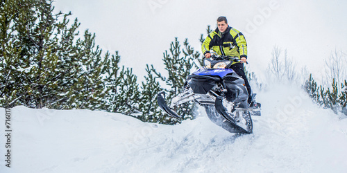 Athlete on a snowmobile moving in the winter forest in the mountains. Man and fast action snowmobile jumping. Jumping on a snowmobile on a background of winter forest. Bright snowmobile