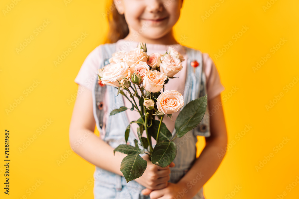 Little girl holding spray roses in her hands against yellow background. Little girl holding spray roses in her hands against yellow background.