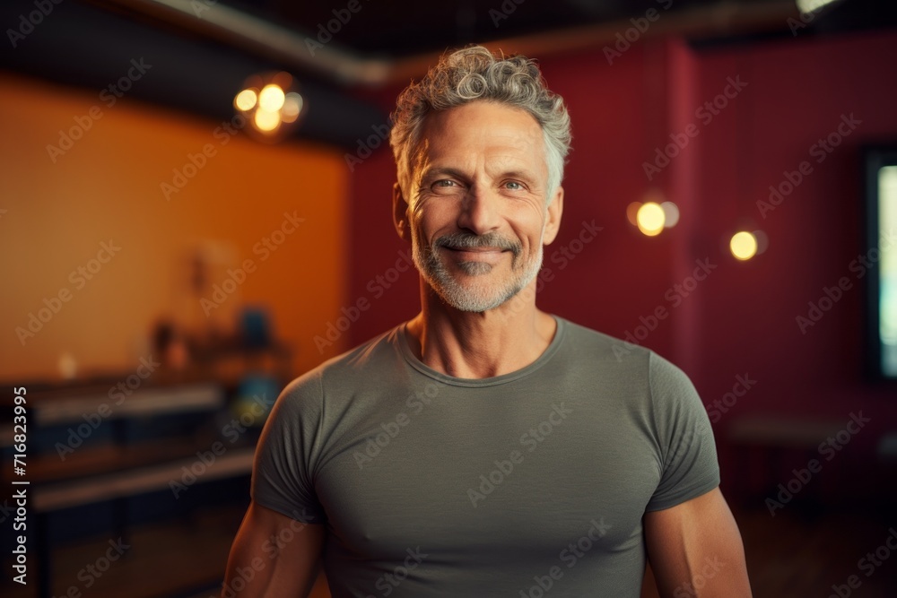 Fototapeta premium Portrait of a happy man in his 50s donning a trendy cropped top against a vibrant yoga studio background. AI Generation