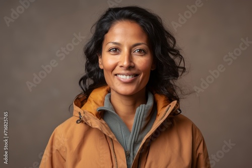 Portrait of a tender indian woman in her 40s sporting a quilted insulated jacket against a pastel or soft colors background. AI Generation