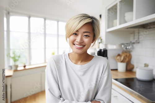 Young smiling Asian woman with short blond hair with blurry kitchen in background