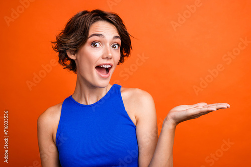 Photo of impressed funky girl dressed blue top open mouth showing arm empty space isolated orange color background